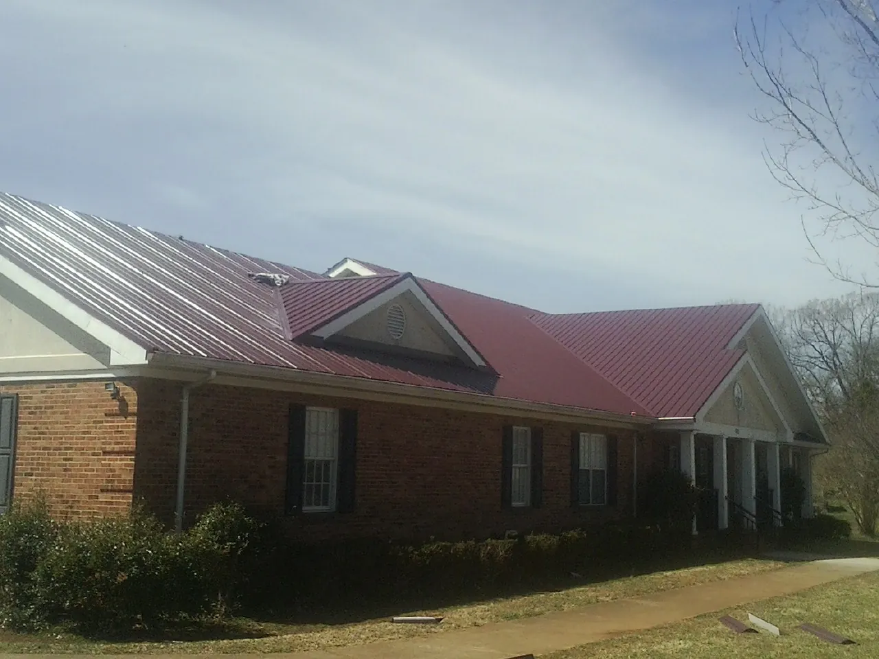 Red metal roof with gabled entries on a long brick building, from a Hail Damage Roof Repair job in Holley
