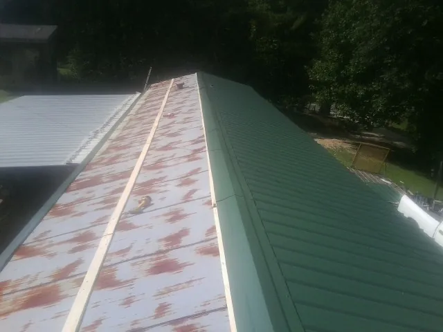 Old rusted panels beside newly installed green metal roofing — Wind Damage Roof Repair by Roofing Brothers in Holley