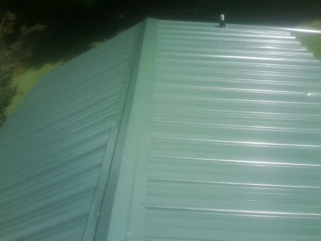 New green metal panels meeting at the ridge of a roof — Flat Roof Repair work by our crew in Holley