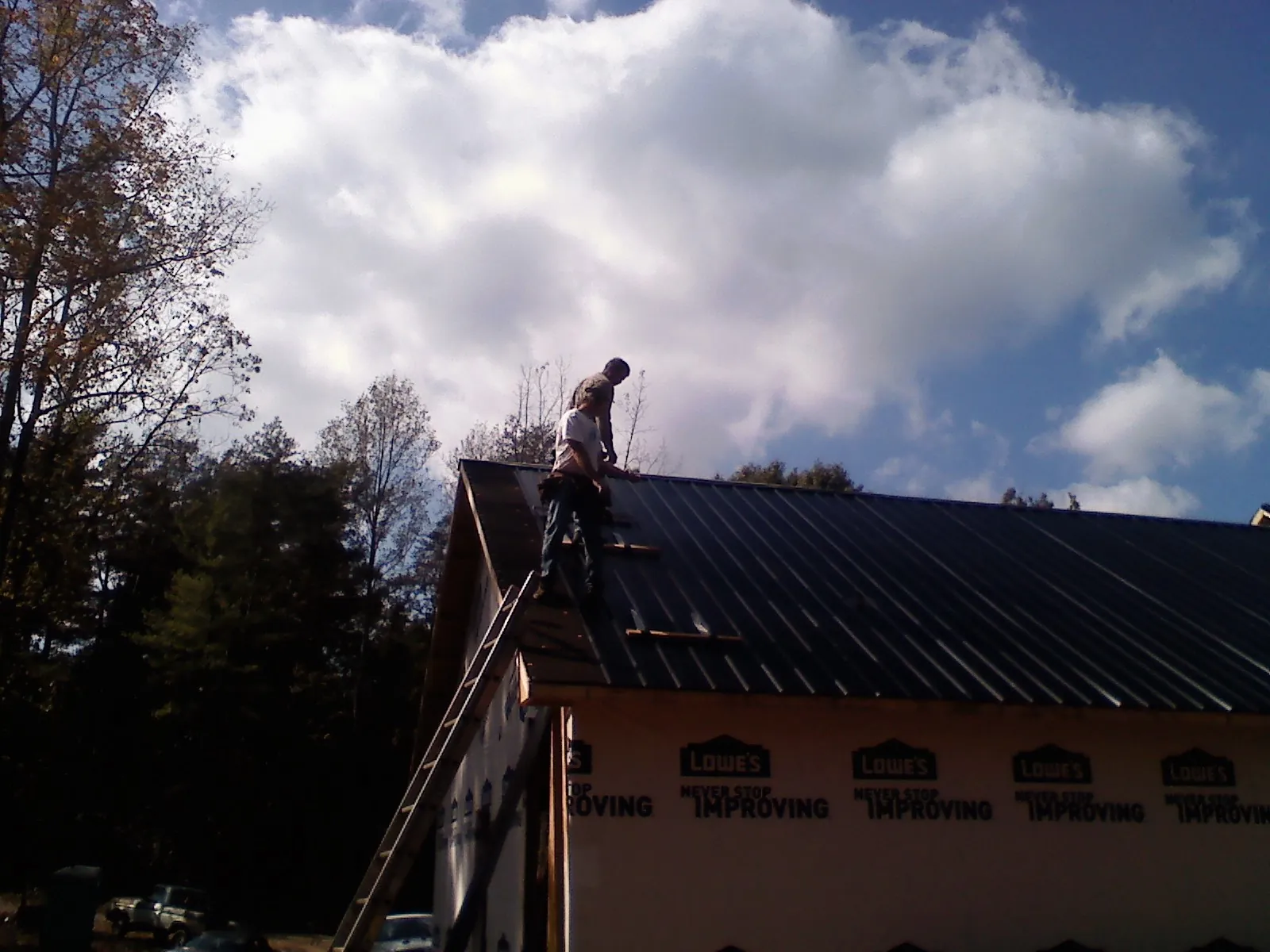 Roofer fastening dark metal panels high against a cloudy sky, from a Roof Inspection job in Holley