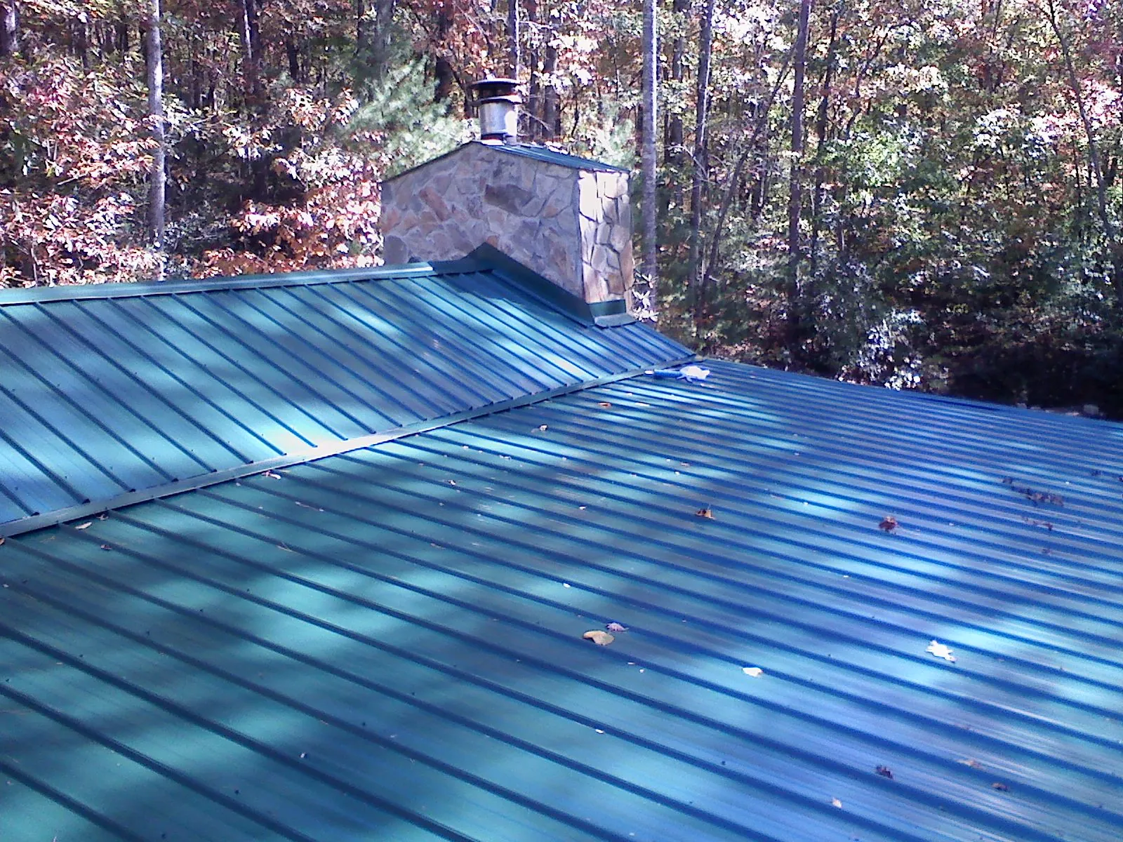 New green metal roof and stone chimney surrounded by autumn woods in Holley