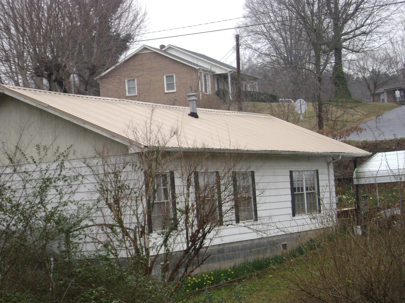 Tan metal roof on a white sided house set into a hillside — Commercial Roofing by Roofing Brothers in Holley