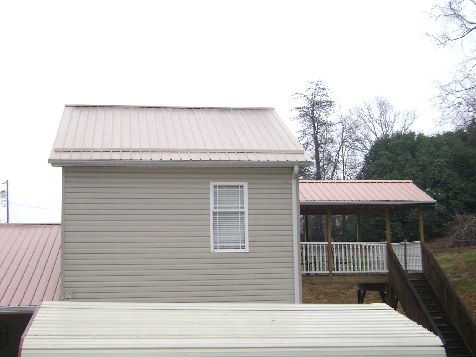Tan metal roofs on a two story addition and attached porch, from a Roof Replacement job in Holley